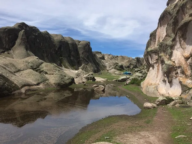 Ein ruhiger Teich, in dem sich felsige Hügel spiegeln, und ein Zelt in Marcahuasi.
