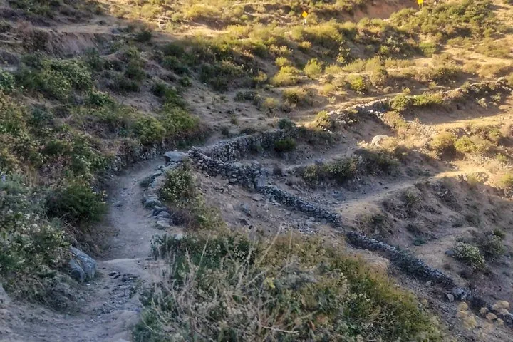 Gewundener Erdweg, der sich in einen steilen Hang gräbt, mit vereinzelter Vegetation.