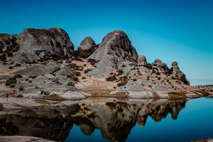 Ruhiger blauer See, der die umliegenden felsigen Hügel und den klaren Himmel perfekt spiegelt.