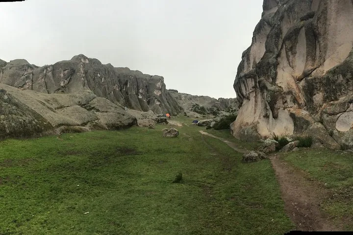 Un valle de hierba rodeado de grandes formaciones rocosas en Marcahuasi bajo un cielo nublado.