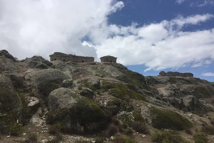 Steinruinen thronen auf einem felsigen Hügel mit Moos und bewölktem Himmel.